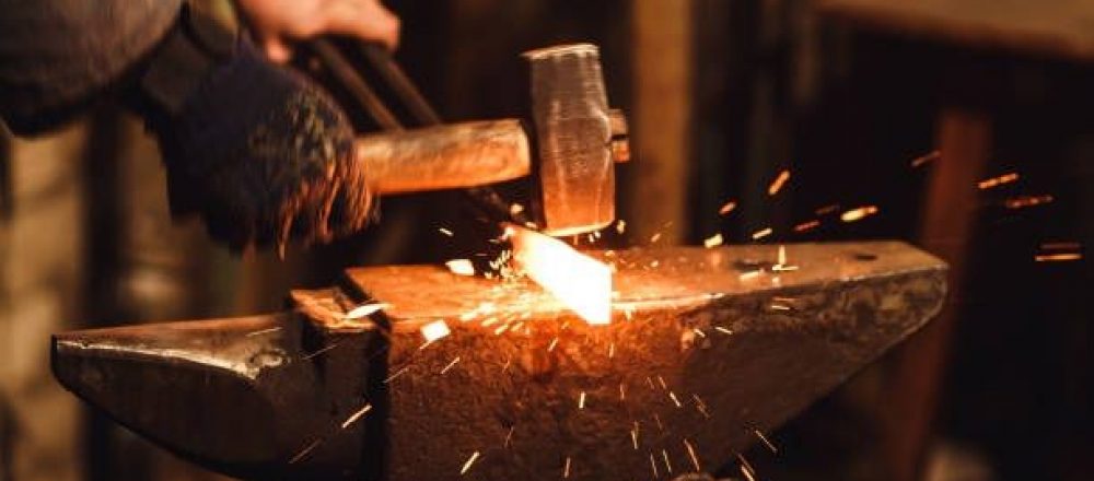 The blacksmith manually forging the red-hot metal on the anvil in smithy with spark fireworks